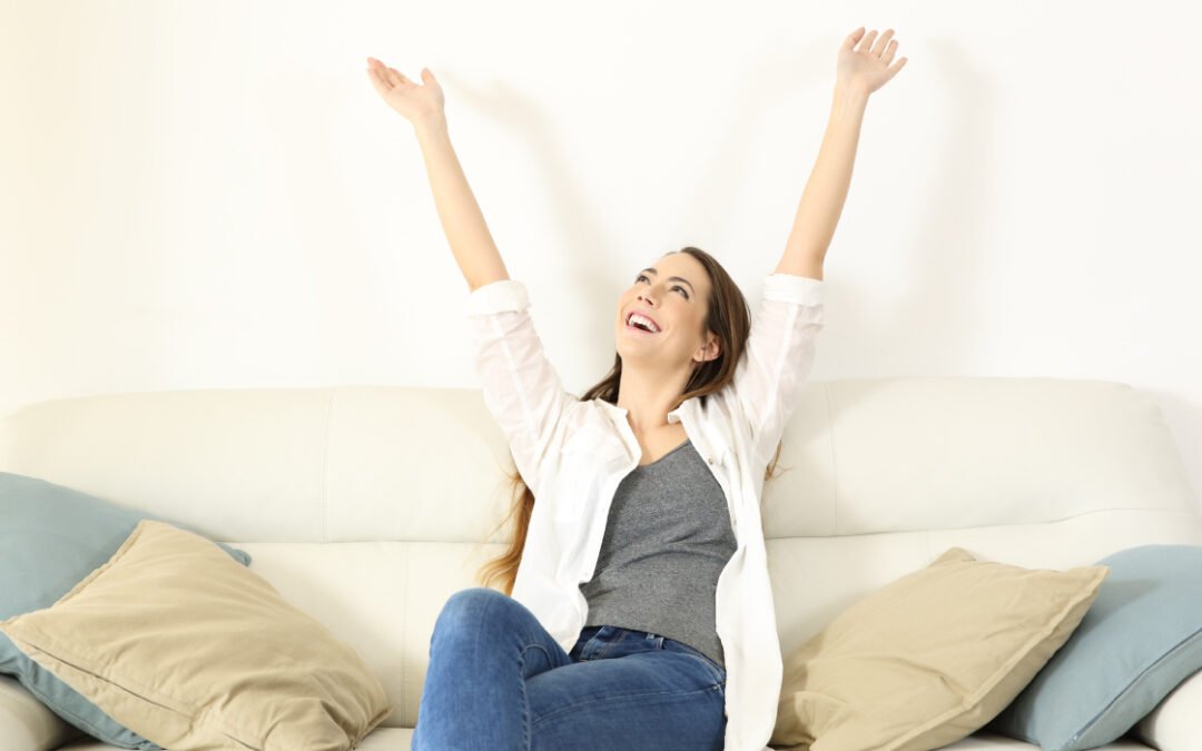 Happy woman on couch celebrating because her home is cooler without high AC costs