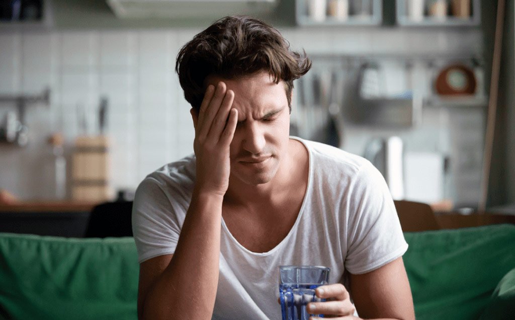 Man holding his head in discomfort while sitting at home, illustrating the potential impact of poor indoor air quality on health, including symptoms like headaches and fatigue.