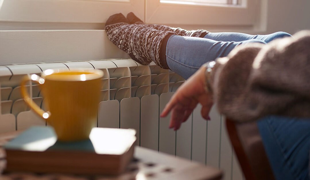 Woman heating feet on a chilly winter day, energy and gas crisis, cold room, heating problems.